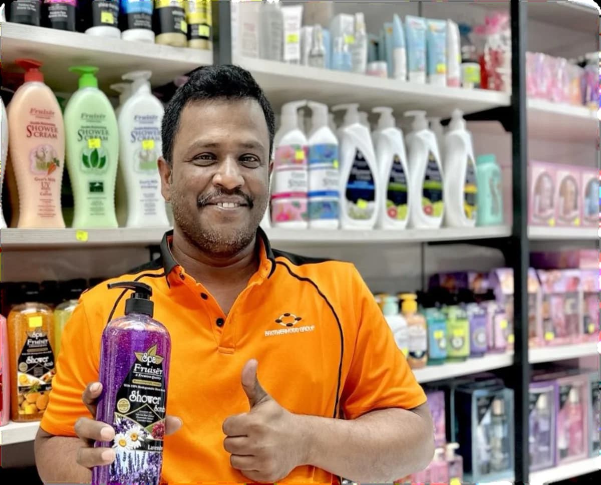 A Brotherhood Group team member in branded uniform holding a shower gel in front of a stocked personal care shelf
